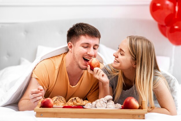 Tiro medio pareja sonriente comiendo en la cama