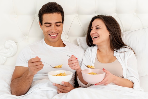 Foto gratuita tiro medio pareja sonriente desayunando en la cama