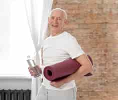 Foto gratuita tiro medio senior hombre sujetando estera de yoga