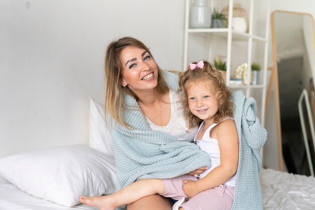 Tiro medio sonriente madre e hija debajo de la manta