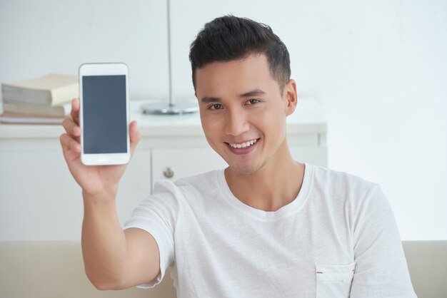 Tiro en el pecho del chico asiático mostrando una pantalla de su teléfono inteligente y sonriendo