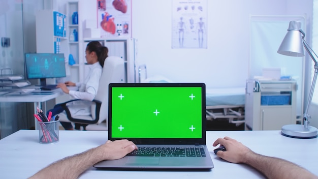 Tiro pov del médico que usa una computadora portátil con chroma key en el gabinete del hospital y un médico que mira la imagen de rayos x. Medic usando portátil con pantalla verde en exhibición en clínica médica.