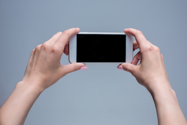 Tiro del primer de una mujer que pulsa en el teléfono móvil en gris.