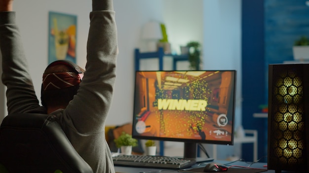 Foto gratuita tiro trasero del jugador de hombre feliz ganando videojuego de disparos en primera persona jugando en una poderosa computadora personal. rendimiento cibernético de transmisión en línea durante el torneo de juegos utilizando tecnología de red inalámbrica