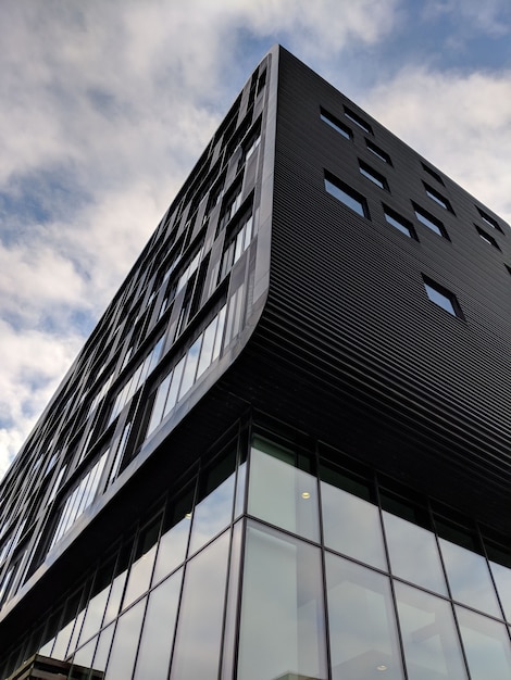 Foto gratuita tiro vertical de ángulo bajo de un edificio negro de gran altura con ventanas de vidrio