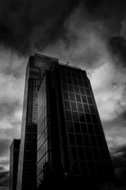 Tiro vertical en ángulo bajo en escala de grises del bloque de la torre con ventanas de espejo bajo impresionantes nubes de tormenta