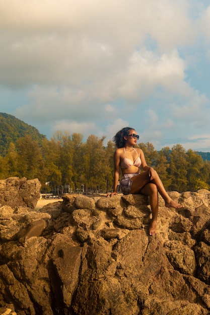 Tiro vertical de ángulo bajo de una mujer sentada en una formación rocosa disfrutando del hermoso día