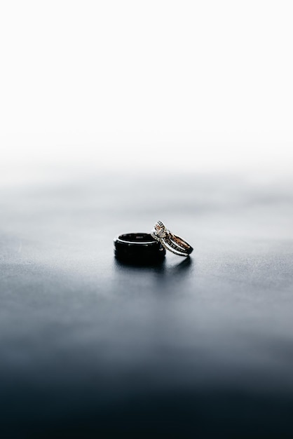 Tiro vertical de los anillos de boda de la novia y el novio en una superficie gris