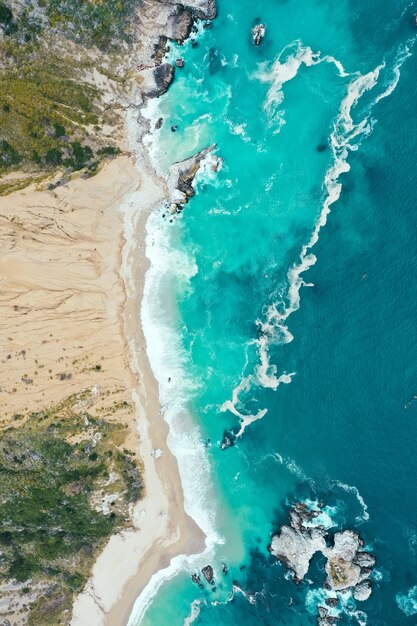 Tiro vertical arriba de la hermosa costa del mar con agua azul limpia y playa de arena