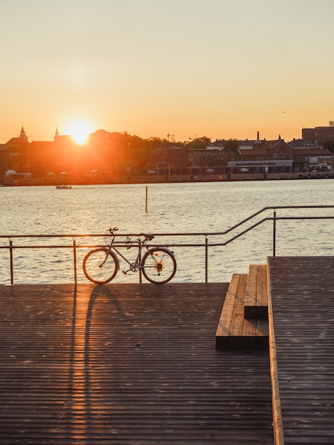 Tiro vertical de una bicicleta estacionada en la orilla del mar cerca del puerto durante la puesta de sol