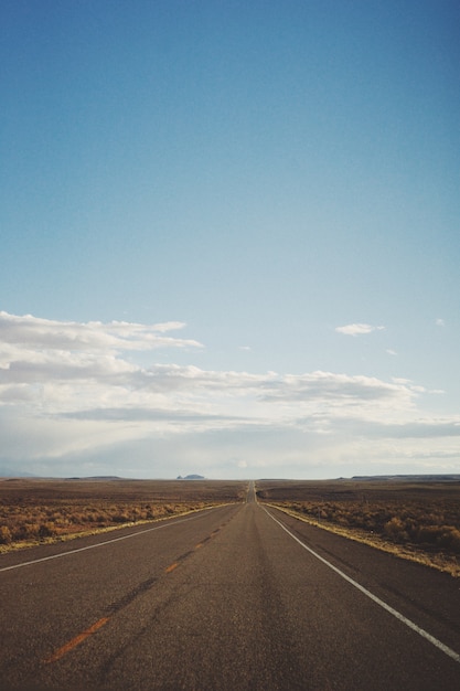 Tiro vertical de una carretera vacía en medio de un desierto bajo un hermoso cielo azul