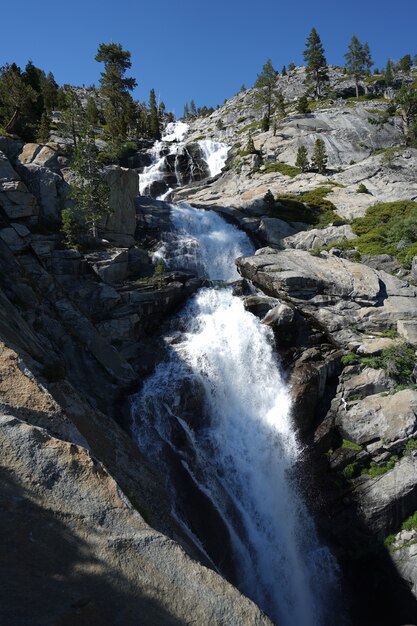 Tiro vertical de una cascada que fluye hacia abajo en los acantilados cerca del lago Tahoe, CA con cielo azul y árboles