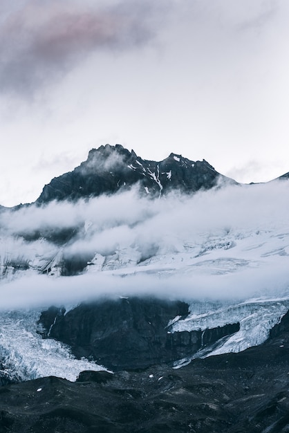 Tiro vertical de la cima de una montaña nevada sobre las nubes con un cielo despejado