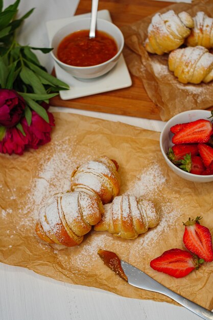 Tiro vertical de croissants recién horneados con fresas y mermelada