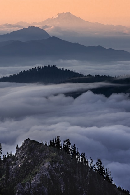 Tiro vertical de montañas sobre las nubes con un cielo naranja