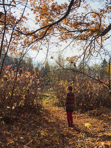 Foto gratuita tiro vertical de una mujer en una boina de pie en el jardín con hojas de otoño caídas