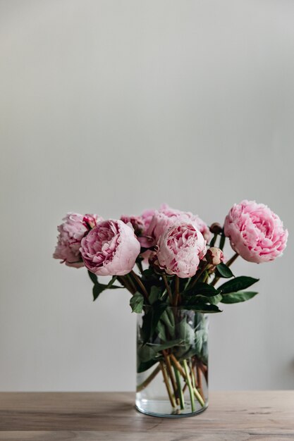 Tiro vertical de peonías rosas con hojas verdes en un florero de vidrio