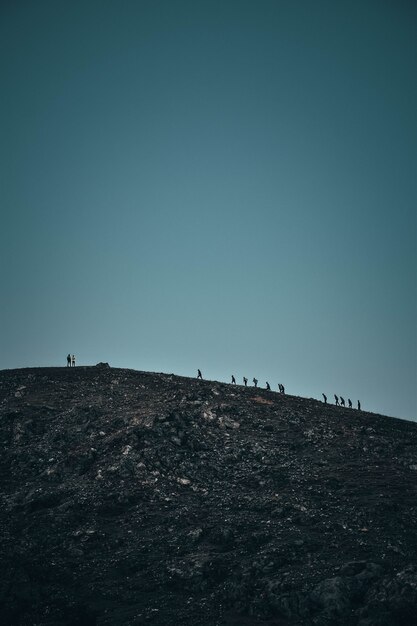 Tiro vertical de personas caminando sobre una empinada colina rocosa en la distancia