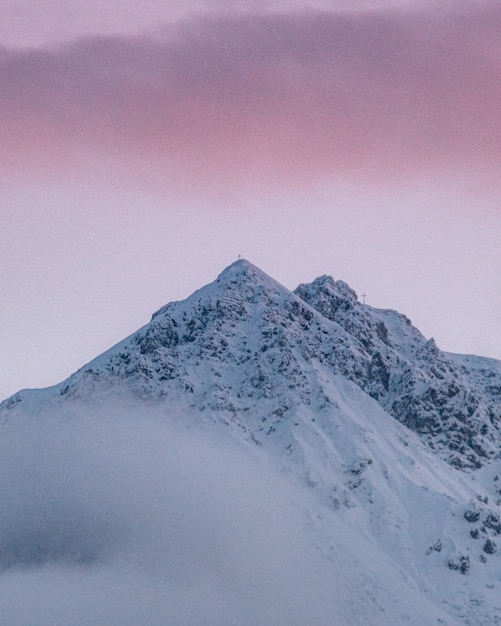 Tiro vertical del pico de la montaña cubierta de nieve bajo el colorido cielo nublado