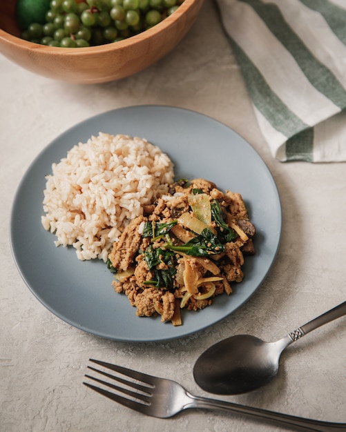 Tiro vertical de un plato lleno de arroz y fideos cerca del tenedor y una cuchara sobre una mesa blanca