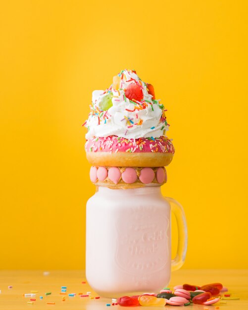 Tiro vertical del primer de un postre con una dona y la crema batida en un tarro para beber