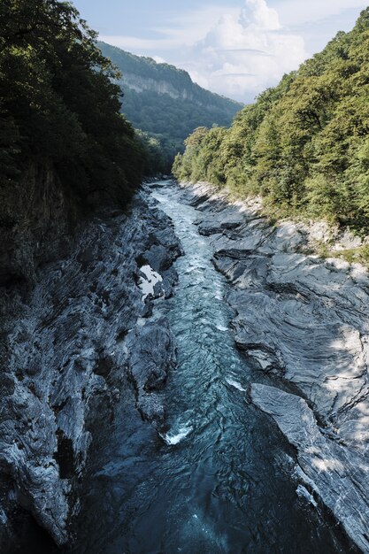 Tiro vertical de un río en medio de acantilados con árboles bajo un cielo azul durante el día