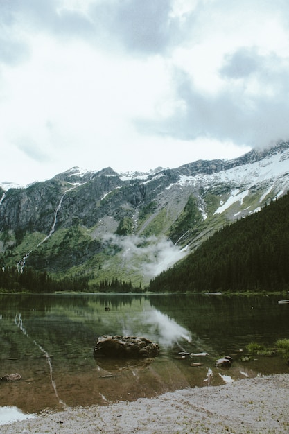 Foto gratuita tiro vertical de una roca en el lago avalanche, con una montaña boscosa