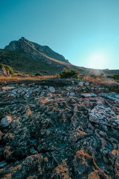 Tiro vertical de rocas cerca de un campo de hierba seca con montaña y un cielo azul claro