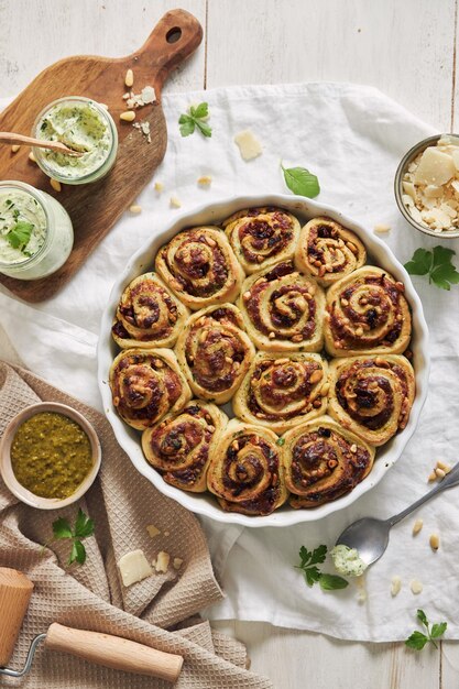 Tiro vertical de rollos de pizza de pesto con piñones y mantequilla de hierbas sobre una mesa blanca