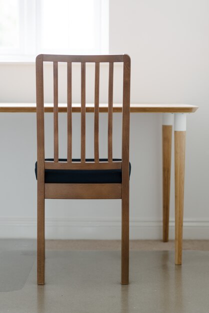 Tiro vertical de una silla de madera y una mesa en una habitación blanca y tranquila