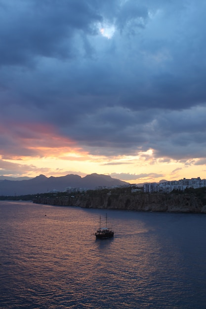 Tiro vertical de un solo barco en el mar bajo las nubes oscuras durante el atardecer