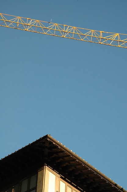 Foto gratuita tiro vertical del techo de un edificio y una grúa con un cielo despejado