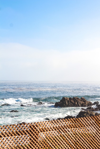 Foto gratuita tiro vertical de una valla de madera cerca de una costa rocosa y un mar