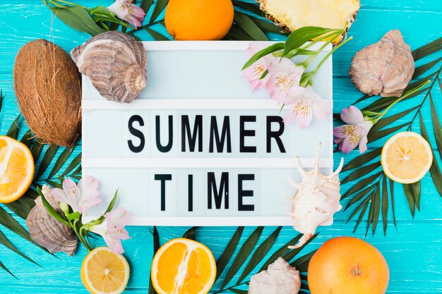 Título del horario de verano en la mesa entre las hojas de las plantas cerca de los frutos con flores