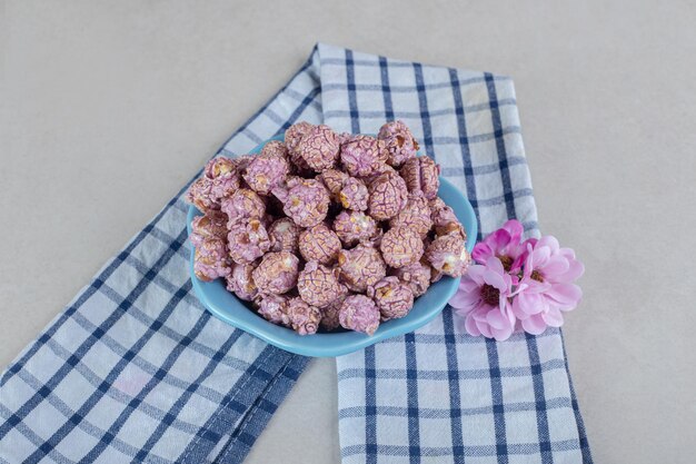 Foto gratuita toalla cuidadosamente doblada debajo de un tazón de dulces de palomitas de maíz y corolas de flores sobre una mesa de mármol.