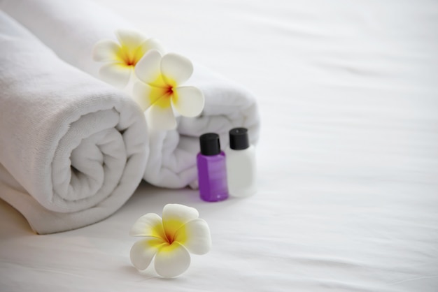 Toalla de hotel, champú y baño de jabón en una cama blanca con flor de plumeria decorada: relájese en el concepto de resort del hotel.