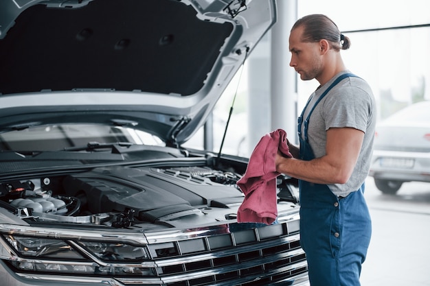 Toalla en manos. Hombre de uniforme azul trabaja con coche roto. Haciendo reparaciones