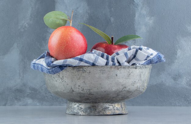 Una toalla y manzanas en un recipiente de metal sobre mármol.