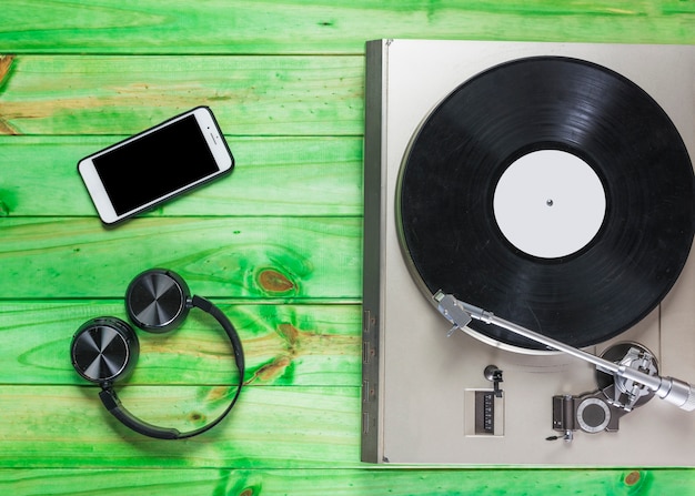 Tocadiscos tocadiscos de vinilo; Auriculares y teléfono celular en fondo de madera verde