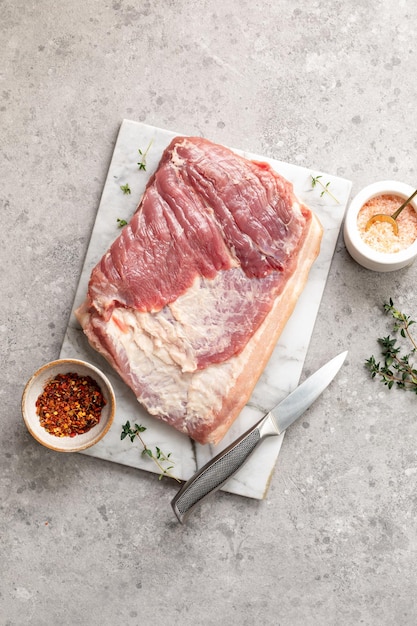 Tocino e ingredientes para hacer porchetta casera Un plato tradicional italiano para las fiestas sobre un fondo de hormigón gris