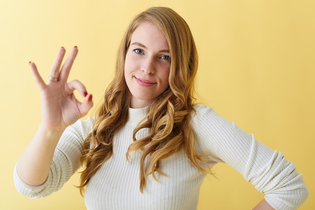 Todo esta bien. Emociones positivas, signos y lenguaje corporal. Atractiva joven de aspecto amistoso sonriendo alegremente y haciendo un gesto aceptable, aprobando una buena idea o disfrutando de una deliciosa cena