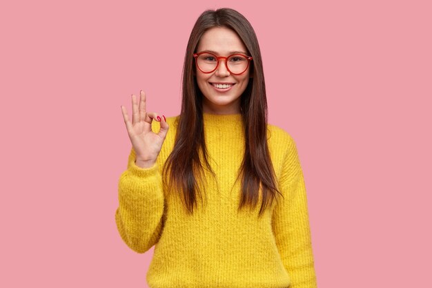 Todo está bien y bajo control. La mujer positiva feliz muestra un gesto bien, demuestra la aprobación de la idea