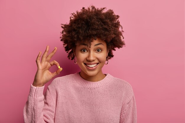 Todo está bien. La linda mujer afroamericana positiva hace un buen gesto, da aprobación, está de acuerdo con algo, usa un suéter informal, dice que sí a las nuevas oportunidades, está complacida con el nuevo concepto