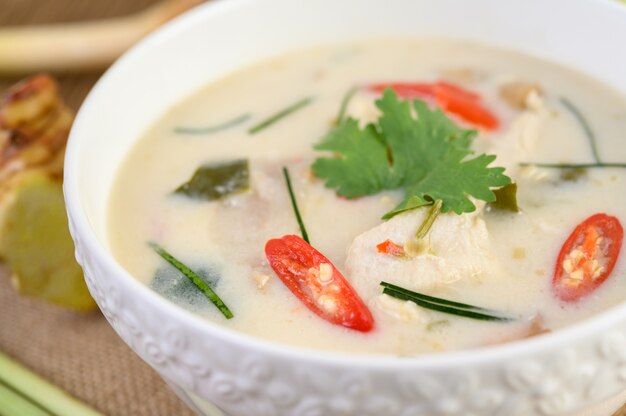 Tom Kha Kai en un tazón con hojas de lima kaffir, hierba de limón, cebolla roja, galanga y chile.