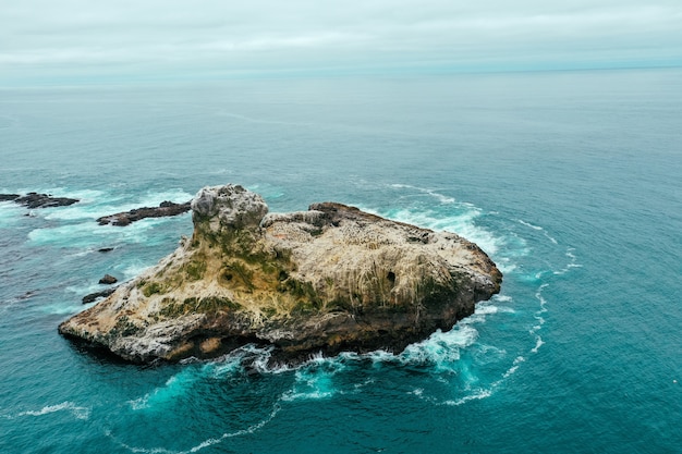 Toma aérea de aviones no tripulados de una pequeña isla rocosa en el hermoso océano azul