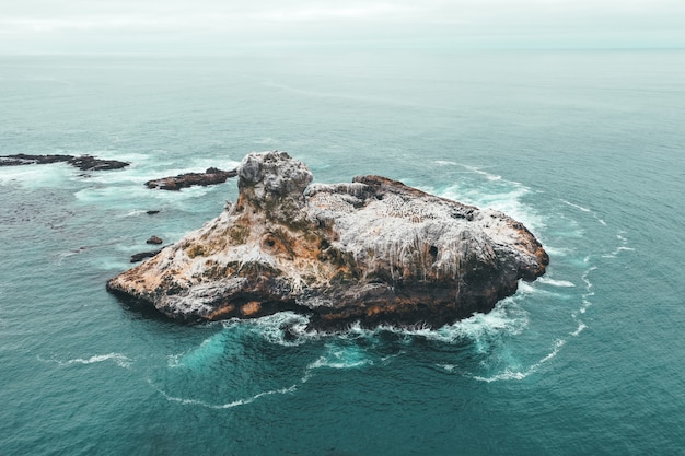 Toma aérea de aviones no tripulados de una pequeña isla rocosa en el hermoso océano azul