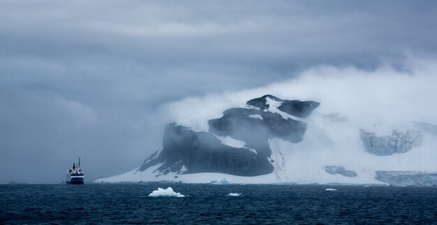 Toma aérea de un barco y un iceberg en la Antártida bajo el cielo nublado