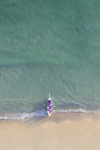 Toma aérea de un barco púrpura en una hermosa orilla bajo la luz del sol
