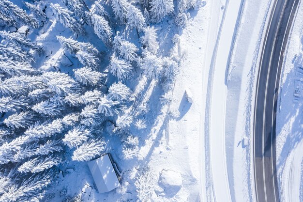 Toma aérea de un bosque con árboles cubiertos de nieve y una carretera de dos carriles al costado