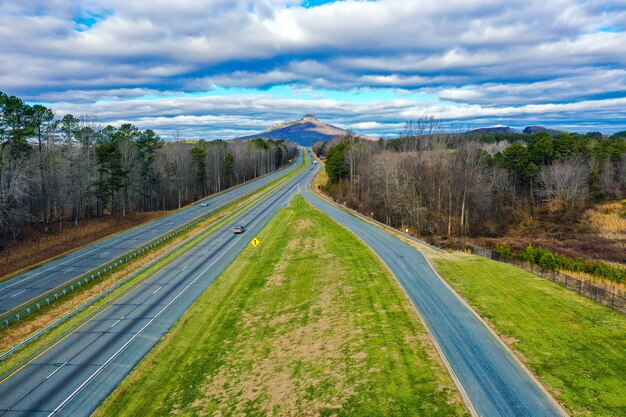 Toma aérea de una carretera con Pilot Mountain en Carolina del Norte, Estados Unidos y un cielo azul nublado